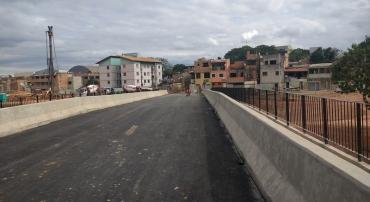 Ponte de concreto e estrutura metálica em bairro urbanizado, durante o dia. 