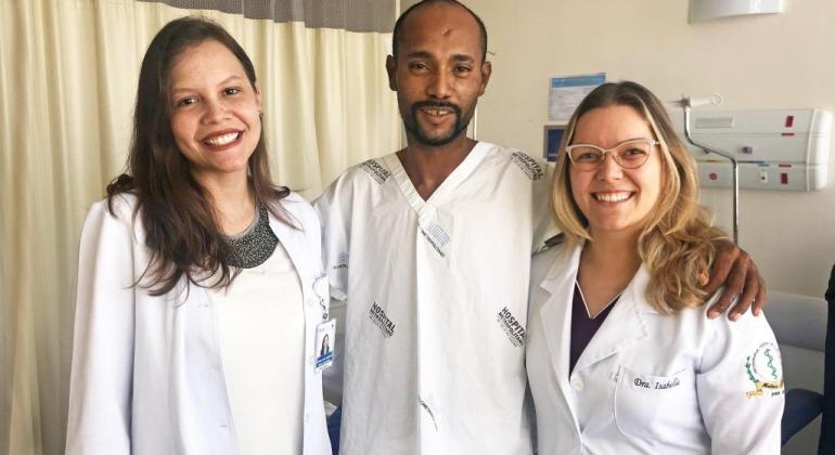 Duas doutoras e um paciente abraçados e sorrindo em quarto de hospital