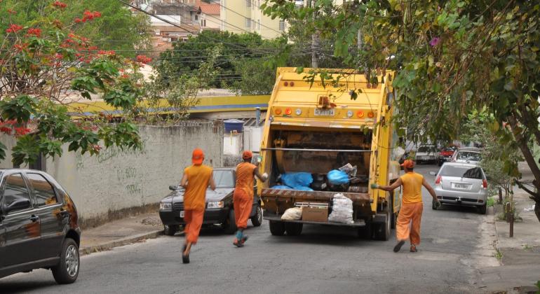 Três lixeiros acompanham o caminhão de lixo e recolhem material nas ruas de Belo Horizonte, durante o dia