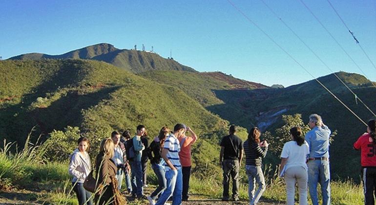 Doze pessoas realizam caminhada em local verde tendo como fundo a Serra do Curral, durante o dia. 