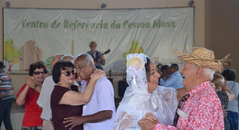 Casais de idosos dançando forró, um deles caracterizado como "Noivos da roça".