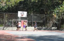 Cinco homens jogam basquete em quadra aberta do Parque Municipal, durante o dia. 