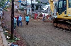 Rua General Osorio, com um declive, sendo pavimentada por máquina. Ao fundo, três pessoas contemplam a pavimentação. 