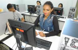 A jovem Kelimara sentada, em frente a um computador, ao fundo, outros três colegas também em frente ao computador.