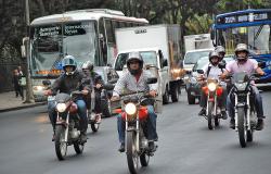 Cinco motocicletas andando em rua em dia de trânsito intenso. 
