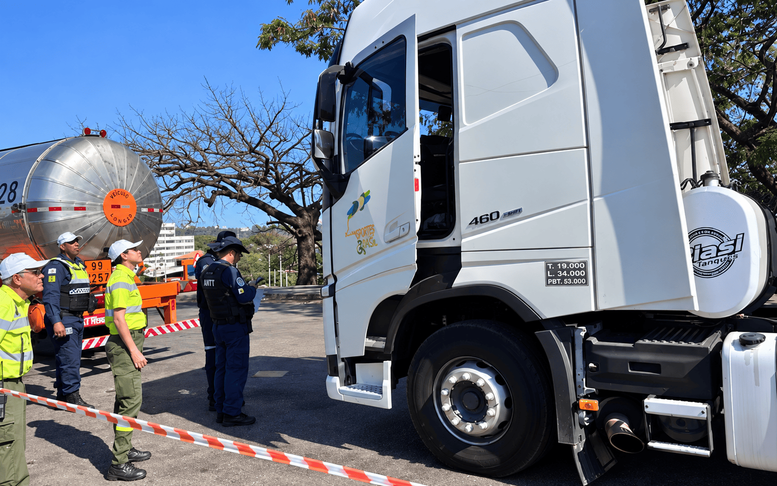 PBH faz nova operação conjunta com a ANTT no Novo Anel para fiscalizar veículos que transportam cargas perigosas A imagem mostra agentes de fiscalização (incluindo elementos da ANTT) a inspecionar um camião cisterna branco numa paragem de controle. Os fiscais vestem fardas e coletes refletores e verificam o veículo e os respetivos documentos junto à cabina aberta, num local delimitado por fita de sinalização.
