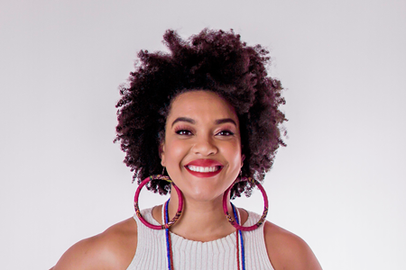 Mulher negra, cabelos curtos, usa camiseta branca e sorri para a foto.