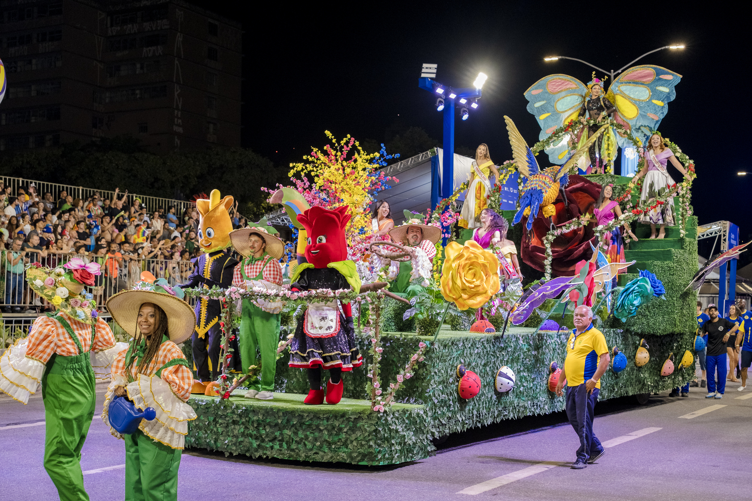 Carnaval de BH é contemplado pela Lei de Incentivo à Cultura para ampliar financiamento em 2027 Desfile da Escola de Samba Estrela do Vale em carro alegórico decorado com flores, folhagens, figuras de animais e personagens coloridos, durante o Carnaval de BH 2026. Integrantes com figurinos típicos e adereços se apresentam diante do público nas arquibancadas, enquanto um homem acompanha o cortejo ao lado do carro.