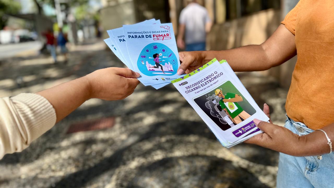PBH oferece gratuitamente tratamento e acompanhamento especializado para quem quer parar de fumar A foto mostra as mãos de duas pessoas segurando panfletos informativos, com orientações sobre os riscos do consumo do tabaco.