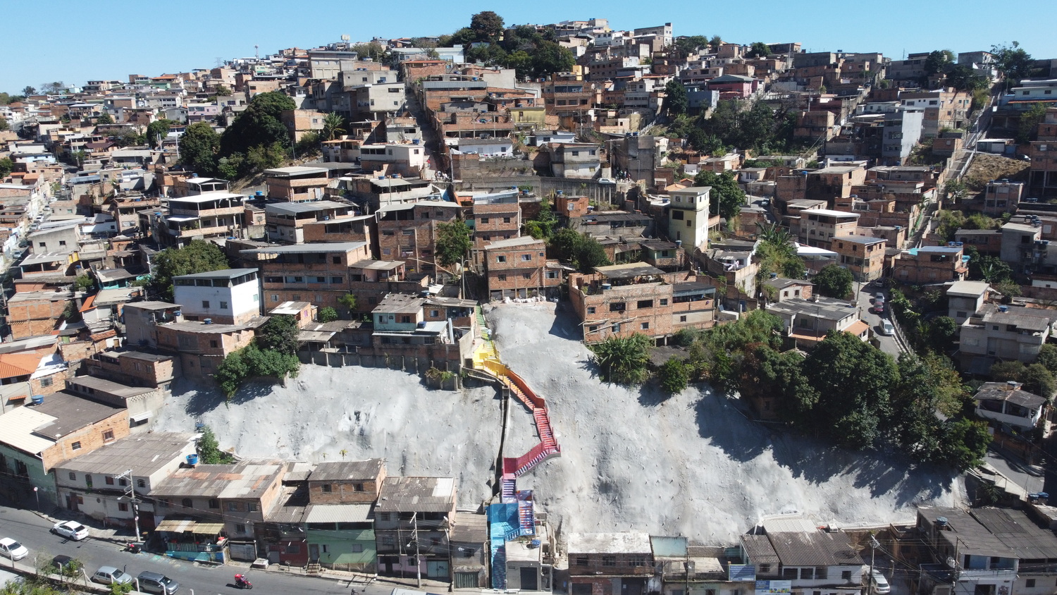 Juventude em Movimento oferece qualificação profissional a 300 pessoas de 14 a 29 anos em situação de vulnerabilidade Imagem aérea da vista parcial do Alto Vera Cruz, com imóveis, muro de contenção de encosta e uma escada de acesso à comunidade.