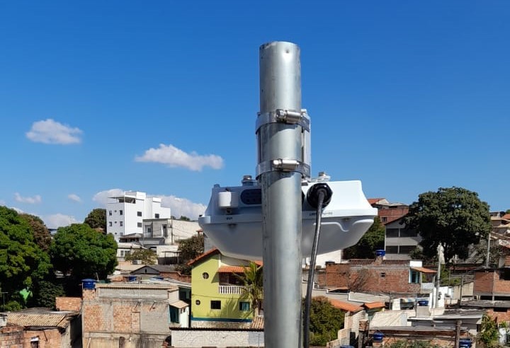 Imagem de uma torre de conexão de internet. Ao fundo, várias casas 