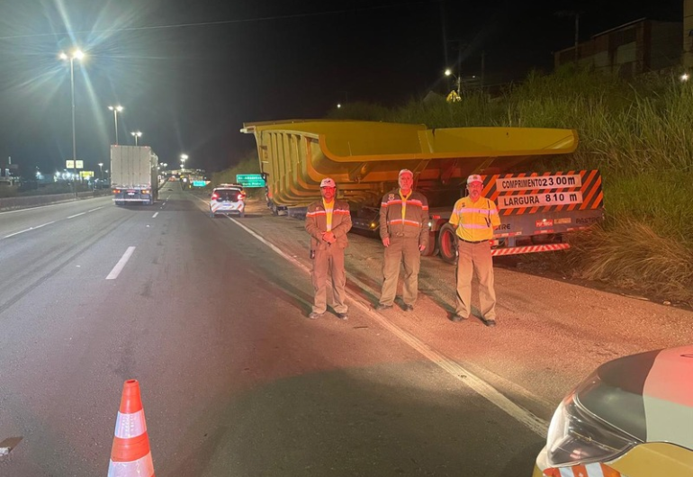 Novo Anel será interditado a partir das 23h30 desta quinta-feira (29) para transporte de carga especial Três agentes da BHTrans usando uniforme, perfilados às margens da riodovia, com veículo de carga atrás