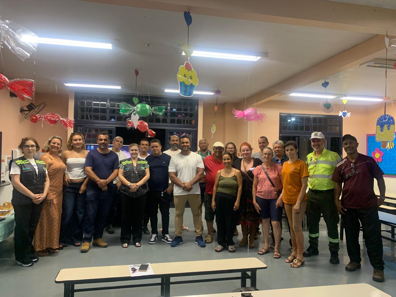 Alterações em circulação de vias e itinerário de linha de ônibus serão debatidas com as Comissões Regionais de Trânsito e Transporte Foto de um grupo de aproximadamente 20 pessoas, entre homens e mulheres, reunidas em pé e lado a lado. Algumas pessoas vestem coletes e uniformes de trabalho, enquanto outras usam roupas casuais. Ao fundo, há janelas, mesas e cadeiras. Todos estão posicionados para a foto.