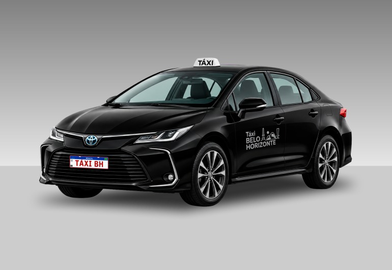 Táxis da categoria Premium deverão atualizar a identidade visual dos veículos Um carro sedã preto, identificado como táxi de Belo Horizonte, aparece de frente e de lado, voltado para a esquerda. O veículo tem quatro portas, vidros transparentes, rodas prateadas e uma placa branca com a inscrição “TÁXI BH”. No teto, há uma placa com a palavra “Táxi”. Na porta dianteira está escrito “Táxi Belo Horizonte”.