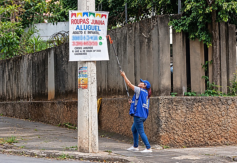 Fiscalização fecha o cerco e apreende quase 1,3 mil faixas irregulares em BH de janeiro a setembro Agente da Fiscalização, usando colete e boné azul, retira cartaz de poste.