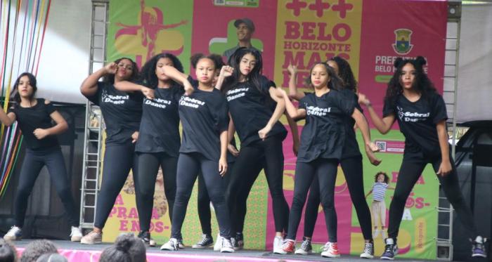 #paratodosverem Descrição: Fotografia colorida de oito meninas estudantes da rede municipal de educação de BH com roupas pretas escrito “Sobral Dance” fazendo apresentação de dança em palco do evento.