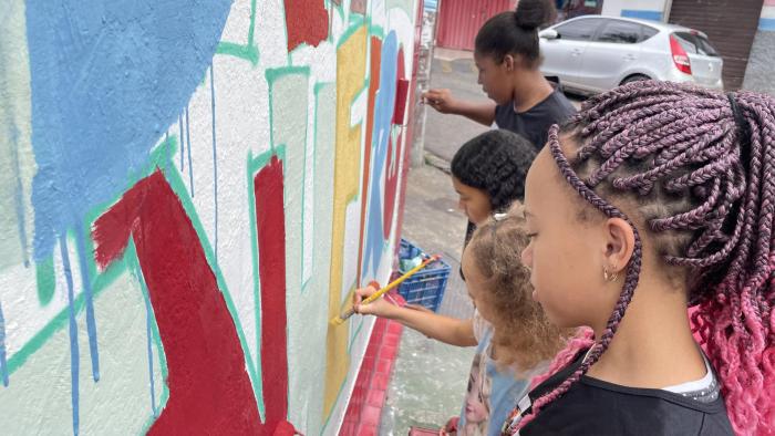#paratodosverem Descrição: fotografia colorida de quatro meninas efetuando pinturas no muro da escola. Foto por: Nathália Ferreira.