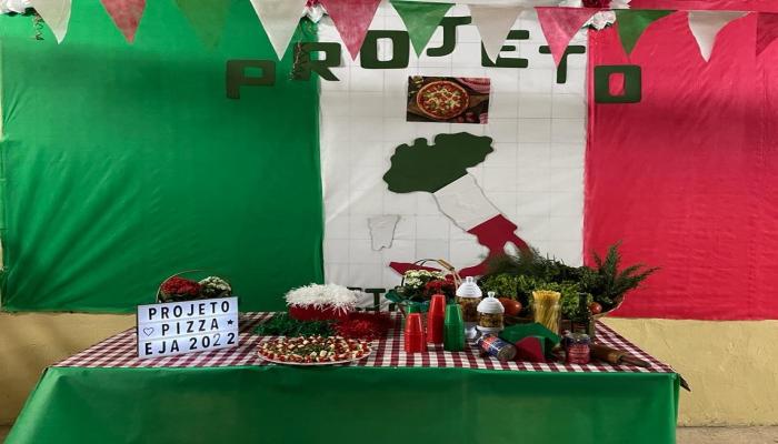  #paratodosverem Descrição: Fotografia colorida de um mural nas cores verde, barnco e vermelho, com os dizeres projeto, e uma mesa enfeitada com as mesmas cores. Foto: Acervo Escola Municipal Milton Campos.