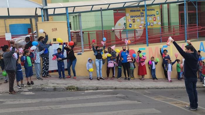 #paratodosverem Descrição: Fotografia contendo crianças e adultos de diversas idades em frente ao muro laranja da Emei. Foto por: Acervo Emei Vila Leonina.