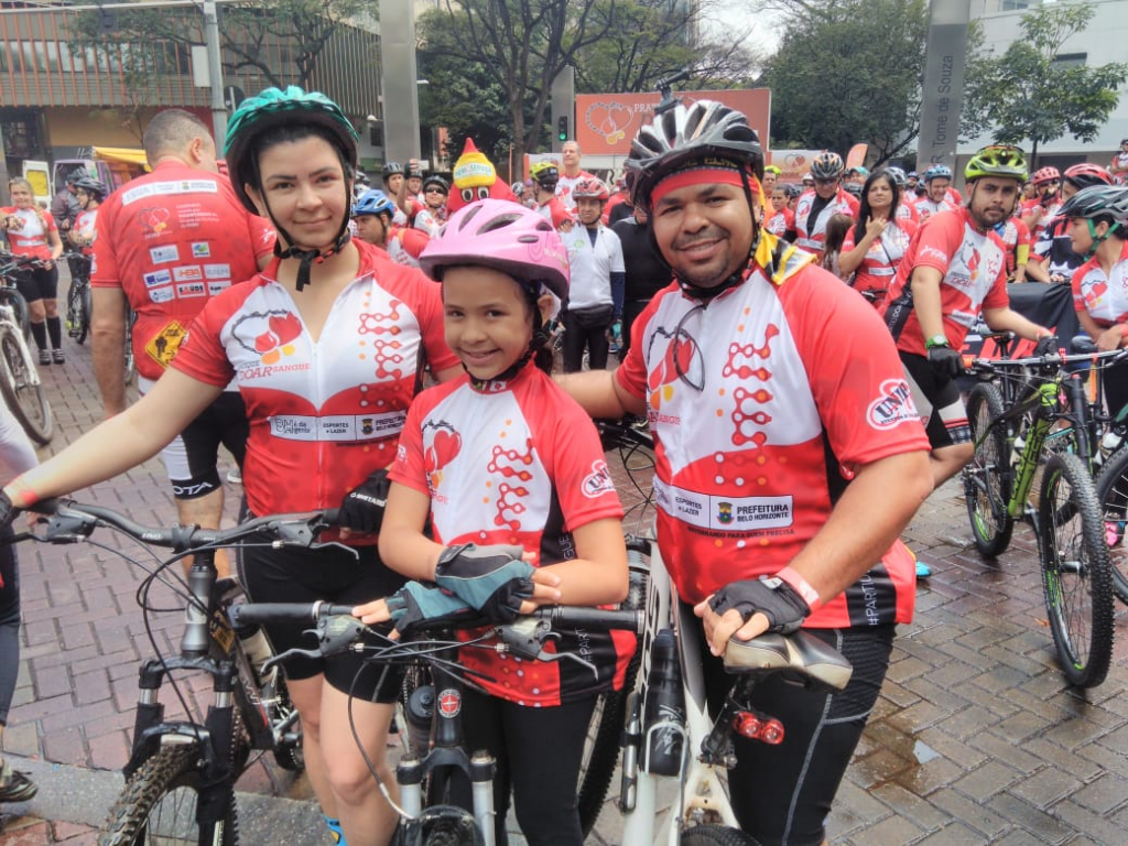 Um homem, uma mulher e uma criança, todos vestindo vermelho segurando bicicletas