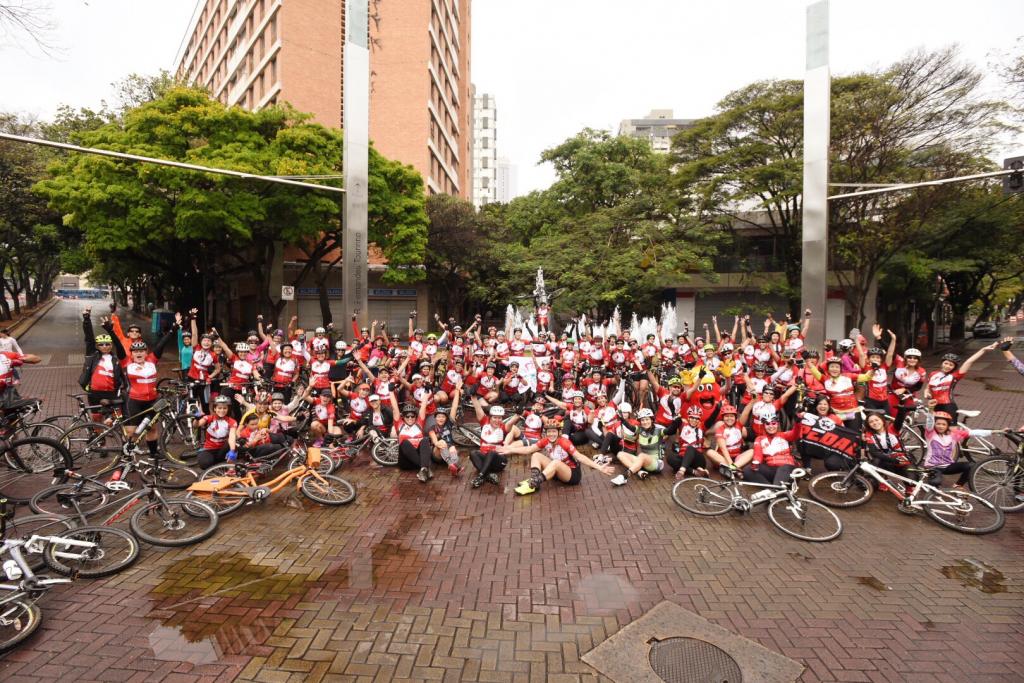 Ciclistas vestindo camisas vermelhas sentados na Praça da Savassi