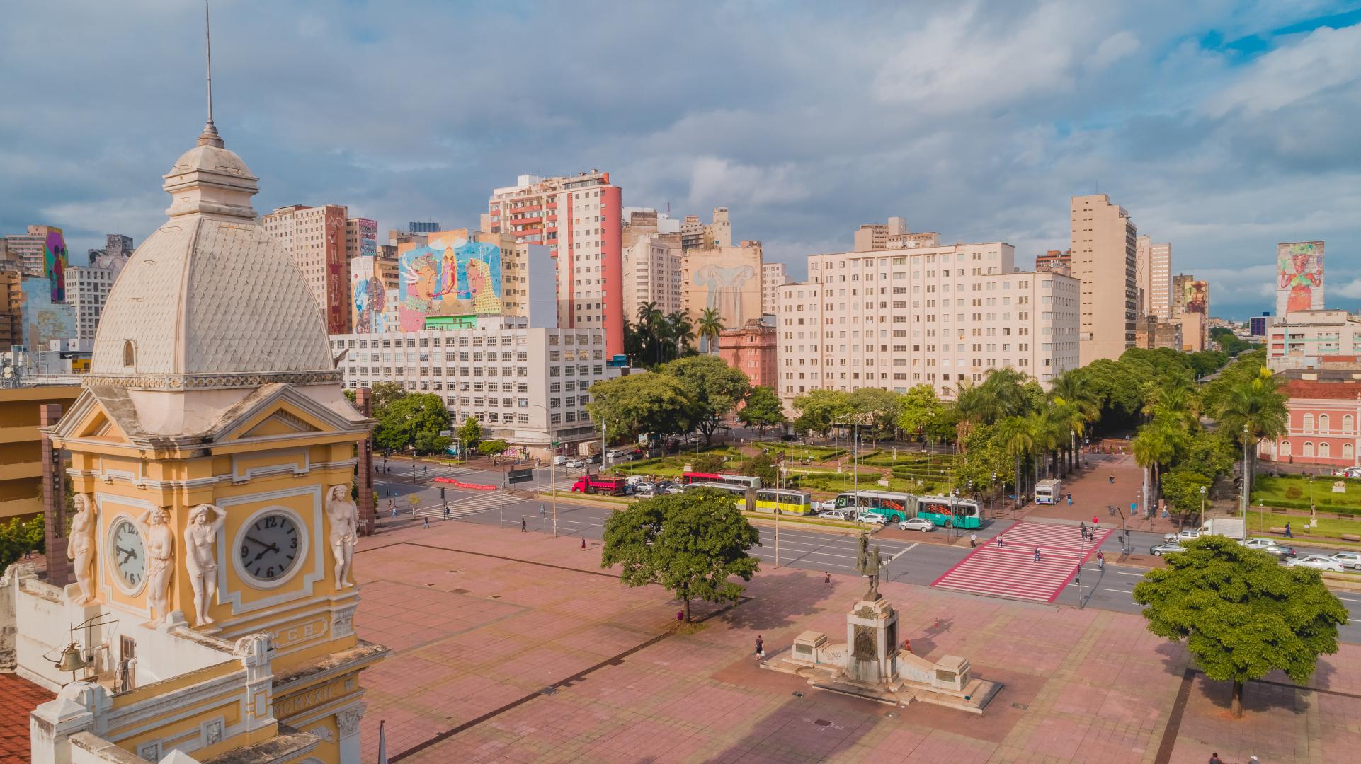 Turismo fomenta economia de BH com mais oferta de experiências em 2026 Vista panorâmica da Praça Rui Barbosa, no Centro de Belo Horizonte, com destaque para o centro da praça, de frente para a Avenida dos Andradas. Em primeiro plano, aparece a torre do antigo edifício da Estação Central, enquanto, ao fundo, prédios comerciais e residenciais compõem a paisagem urbana. A imagem também mostra áreas arborizadas, faixas de pedestres, veículos e ônibus em circulação, sob um céu parcialmente nublado.