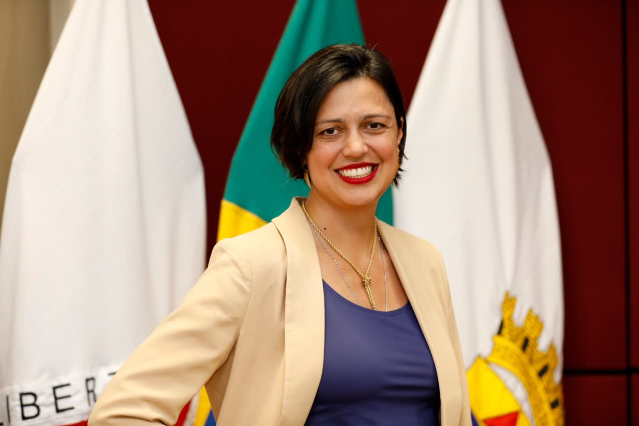 Júlia Gallo, Subsecretária de Assuntos Estratégicos da Secretaria-Geral Mulher de cabelo preto, blusa azul e blazer creme, sorrindo.