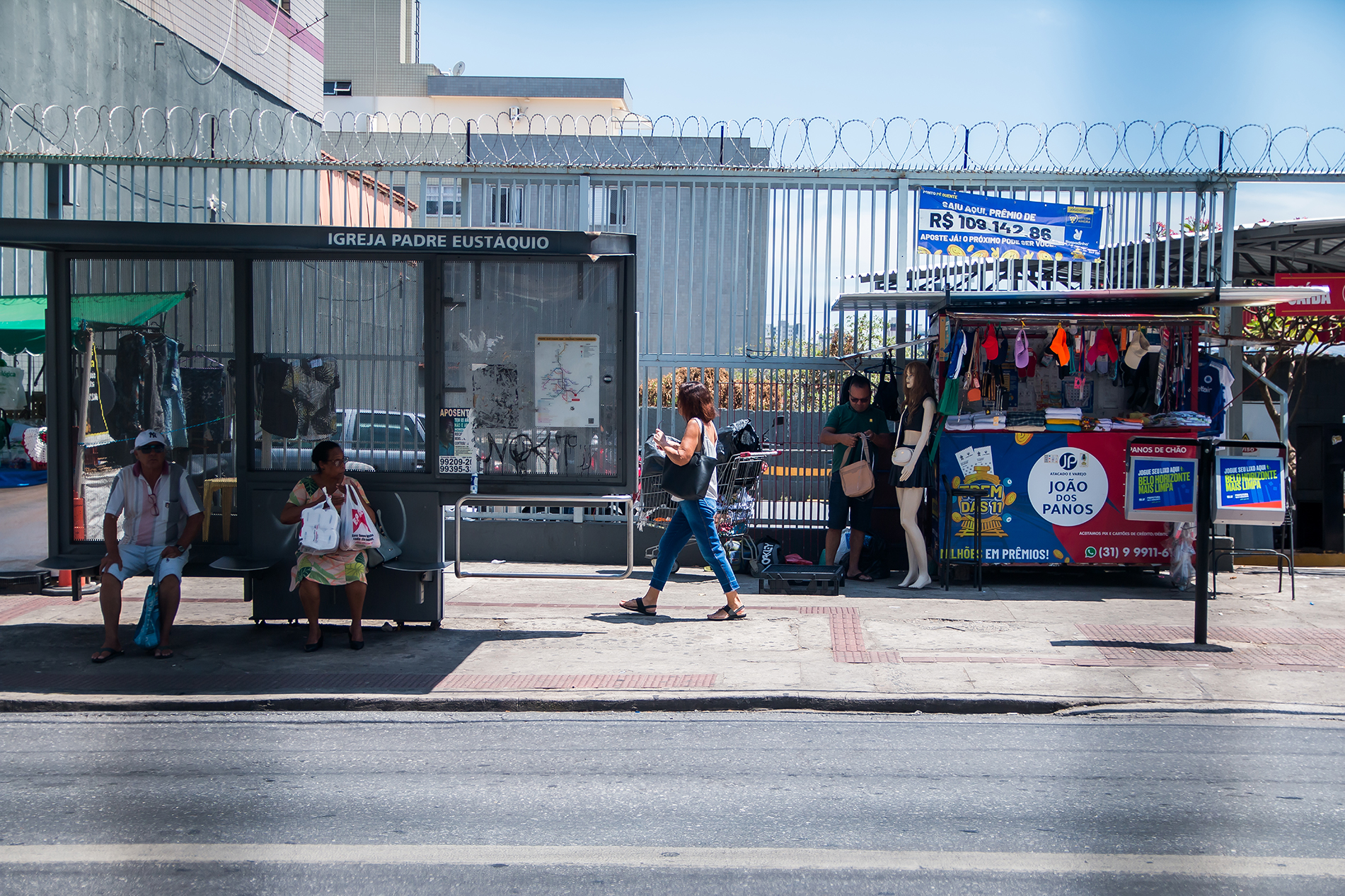 Ponto de ônibus na padre eustáquio com um vendedor de bolsas ao lado.
