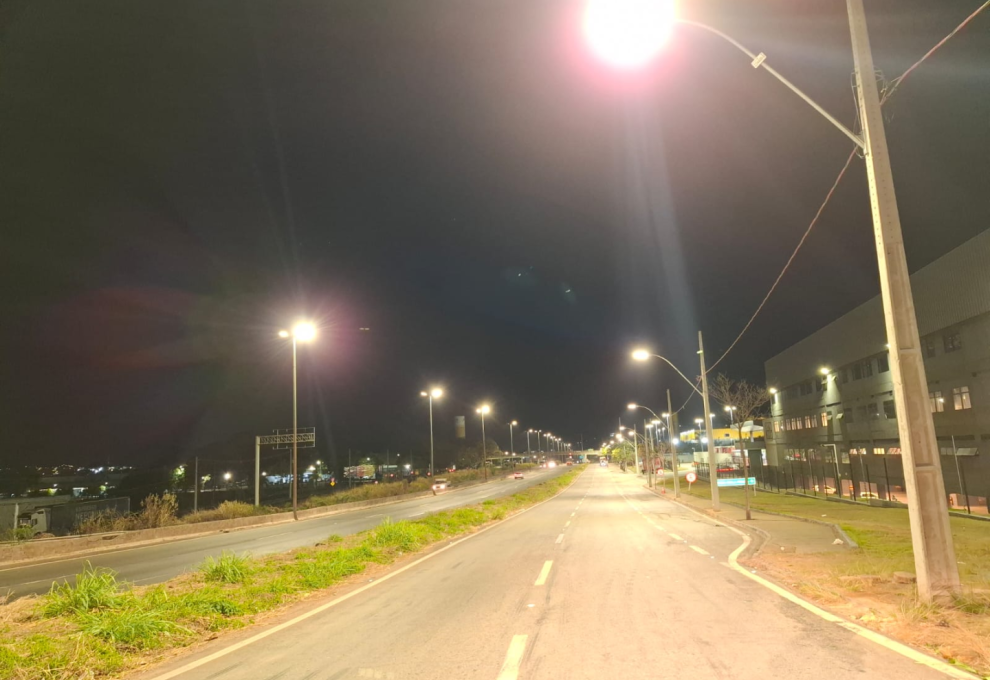 Prefeitura de BH amplia a infraestrutura da iluminação em trechos do Novo Anel em duas regionais Imagem de uma via vazia, no período da noite, com canteiro no meio, iluminada por poste.