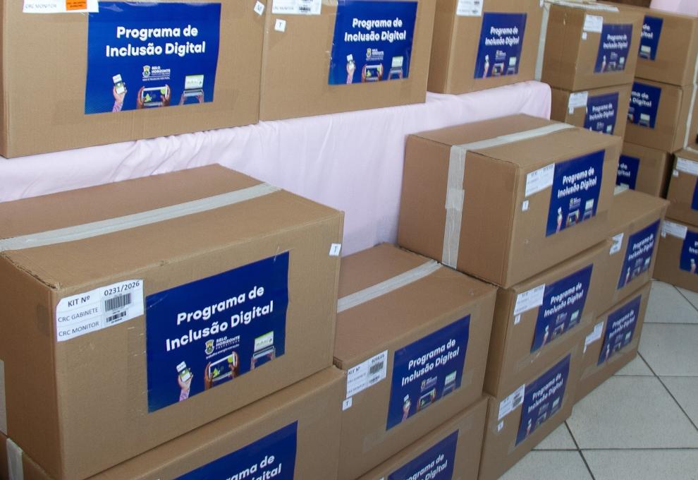 PBH amplia inclusão digital com mais de 500 computadores doados em 2026 Caixas empilhadas com computadores na cor parda com adesivos em azul escrito Programa de Inclusão Digital