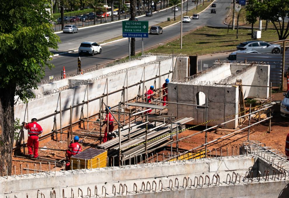 Prefeitura de BH realiza operação especial para nova etapa das obras do Trevo do Belvedere Operários vestidos de uniforme vermelho trabalham no canteiro de obras do Trevo do Belvedere, com a rodovia ao fundo