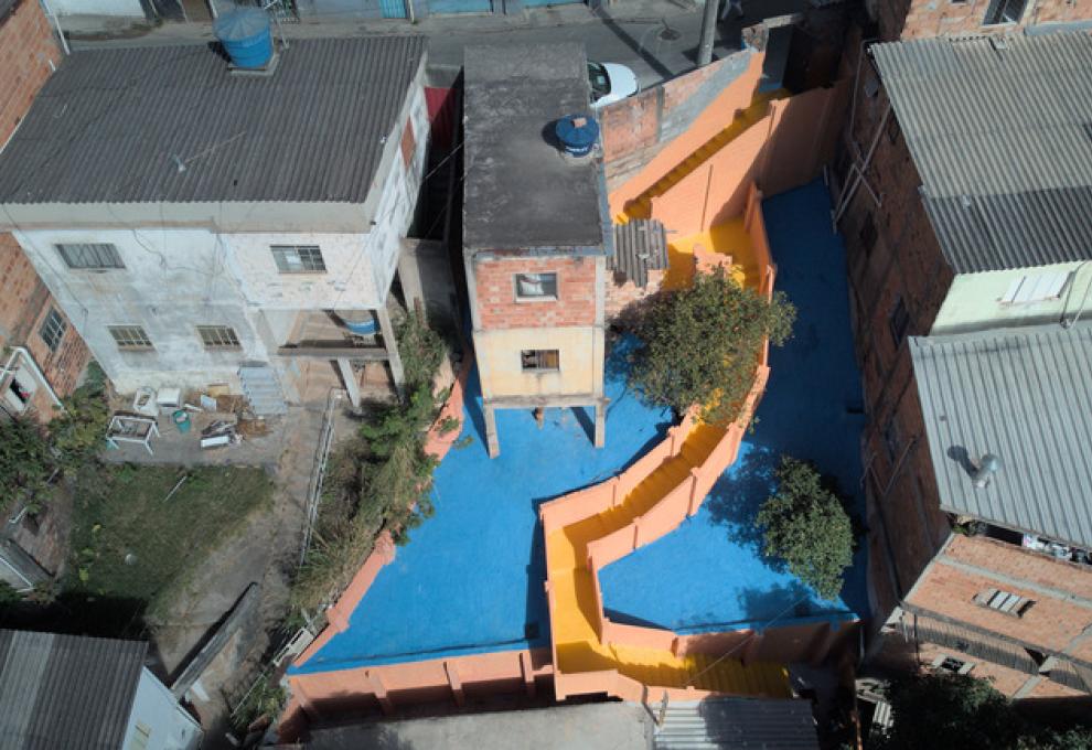 PBH conclui obra de contenção de encosta e amplia segurança na Vila Nossa Senhora de Fátima Imagem aérea de trecho reformado no Aglomerado da Serra. Escadaria pintada de amarelo comparte o pátio pintado de azul.