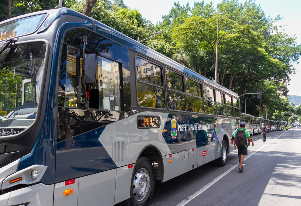 Ônibus novo da Prefeitura de Belo Horizonte para em uma rua em diagonal na foto. Árvores ao fundo, ambiente aberto, céu azul e limpo. 