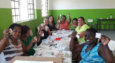 Grupo de mulheres em mesa mostrando bijuterias que fazem