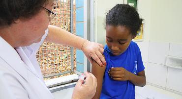 Assistente de saúde vacina criança de cerca de nove anos. 