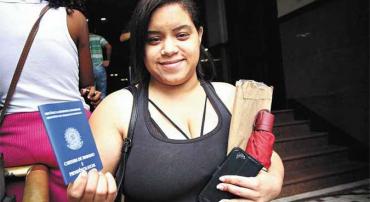 Uma jovem com a carteira de trabalho em mãos em frente ao SINE