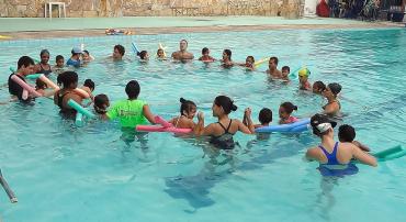 Cerca de 14 crianças do Programa Superar fazem círculos com bóias em piscina, acompanhados por monitores.