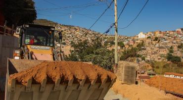 Trator carregando terra em Obra na Vila Fazendinha, ao fundo, comunidades do aglomerado da Serra.