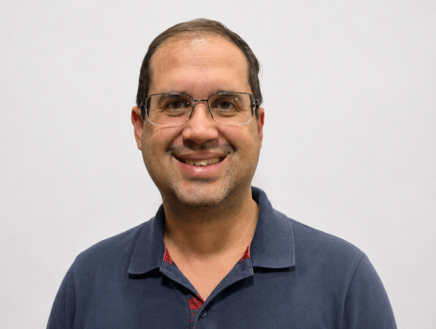 Alexandre Lopes Vieira Homem de aparência simpática e sorridente, com cabelo curto e escuro, óculos de armação fina e barba. Veste uma camisa polo azul-marinho e está posicionado em frente a um fundo claro, transmitindo uma imagem profissional e acolhedora.