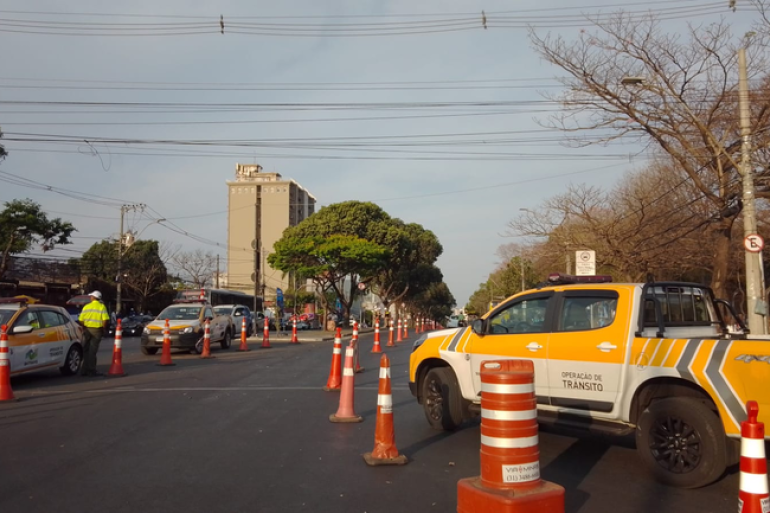 Via com sinalização, cones laranjas e um carro amarelo e branco da BHTrans 