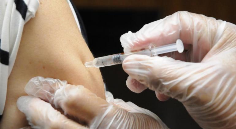 Prefeitura recebe nova remessa de vacinas e retoma imunização contra a gripe Imagem de um profissional da saúde aplicando vacina contra a Influenza no braço de uma pessoa