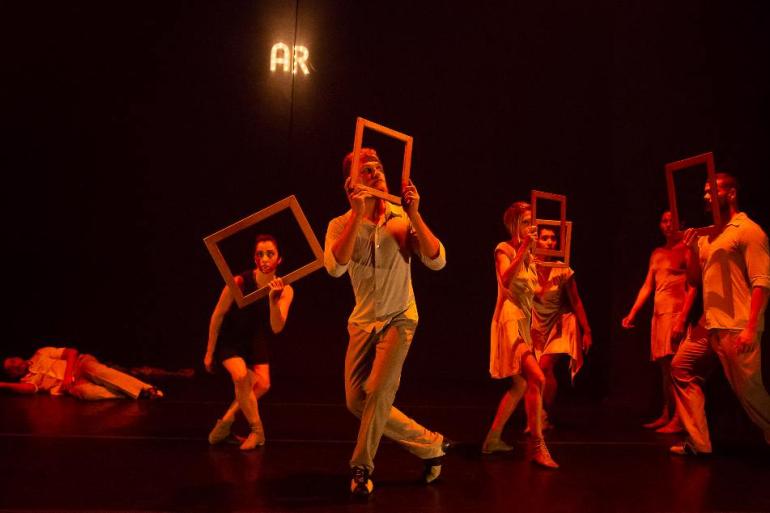 Remontagem de “Âmago” chega ao Teatro Francisco Nunes com ingressos a partir de R$ 1 Grupo de bailarinos num palco escuro e com iluminação em tons quentes de laranja e vermelho. Vários bailarinos seguram molduras de quadros retangulares vazias à frente dos rostos ou corpos, em poses dramáticas de dança contemporânea. Ao fundo, no topo, lê-se a palavra "AR" iluminada, e no chão, à esquerda, um bailarino surge deitado.
