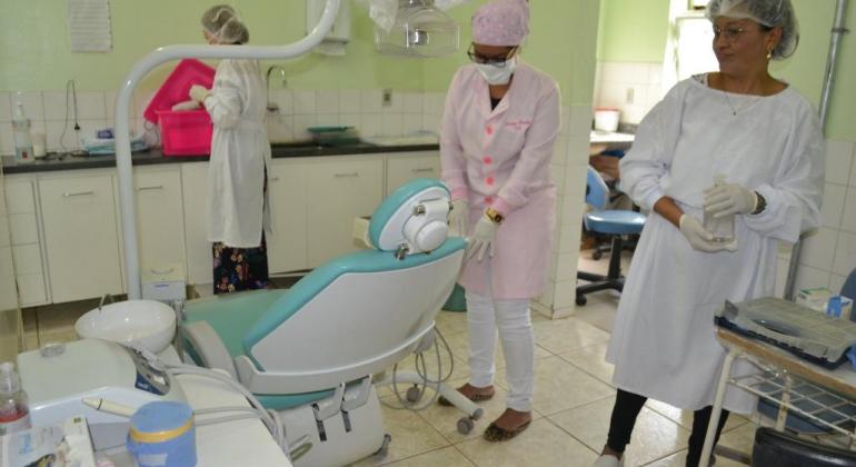 Consultório odontológico em centro de saúde com equipamentos novos, um dentista e duas técnicas. 