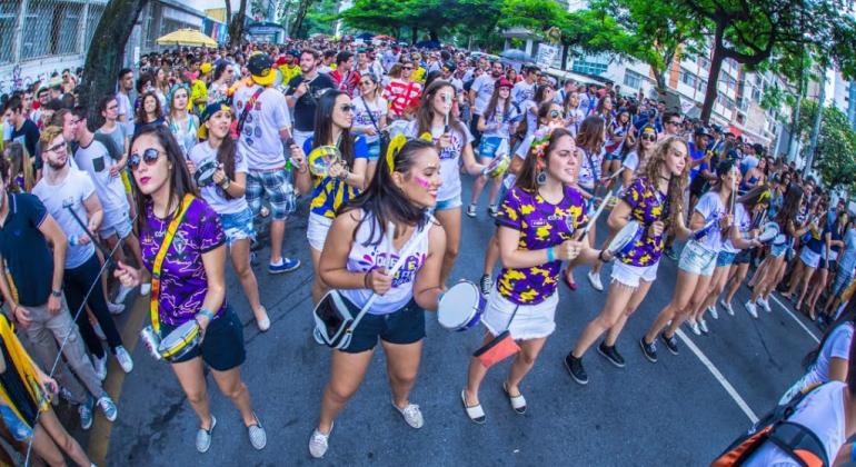 Quatro mulheres tocam instrumentos de percussão á frente de bloco carnavalesco; imagem ilustrativa.