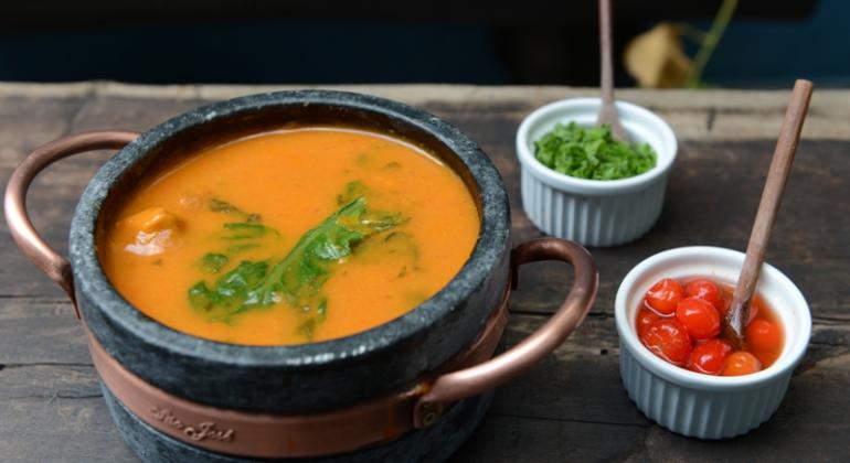 Panela com caldo e duas tigelas, uma com cheiro verde e uma com tomate