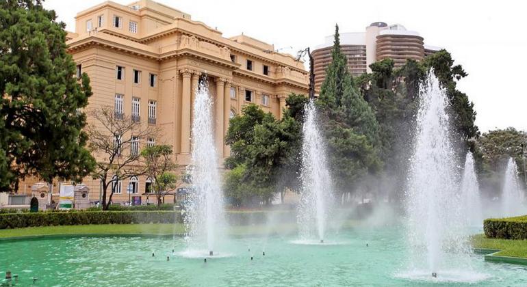 Fonte de água da Praça da Liberdade com prédio ao fundo, durante o dia. 