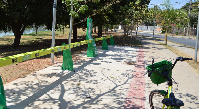 Bicicleta com cestinho e cores fortes próxima a estação de compartilhamento em calçada de BH, durante o dia. 