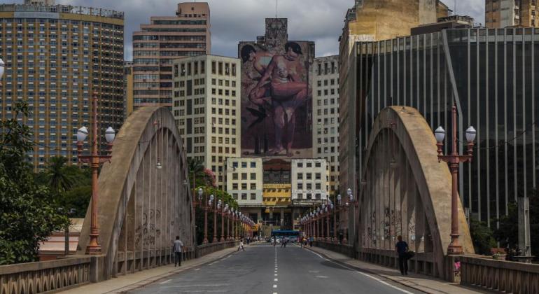 Fachada de Prédio dom imagem de duas mulheres pintada ao fundo de Viaduto Santa Tereza, durante o dia