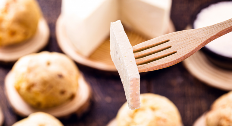 Um pedaço de queijo fisgado pelo garfo e uma mesa de café