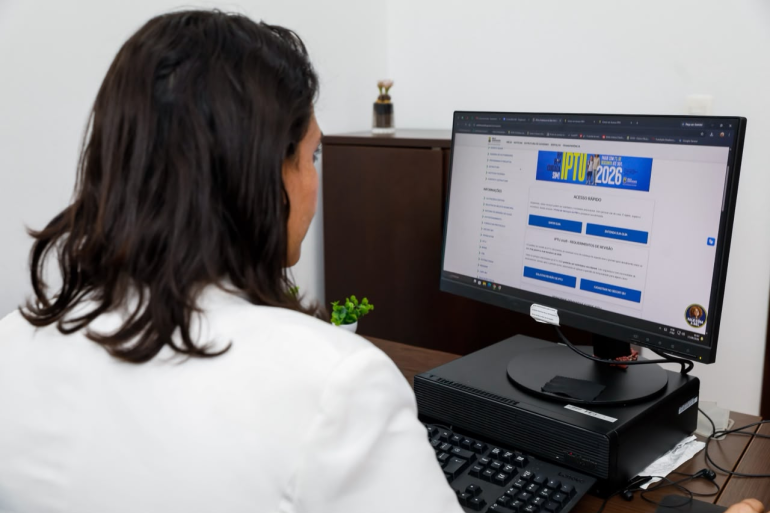 Referência na desburocratização dos serviços, PBH chega a 3,5 milhões de solicitações pelos canais digitais Mulher com uma blusa branca sentada em frente ao computador com o portal de serviços da PBH na tela.